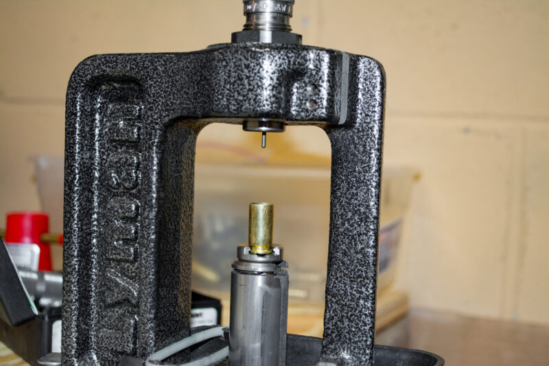 The resizing step. The press piston drives the case into the fixed resizing die.
